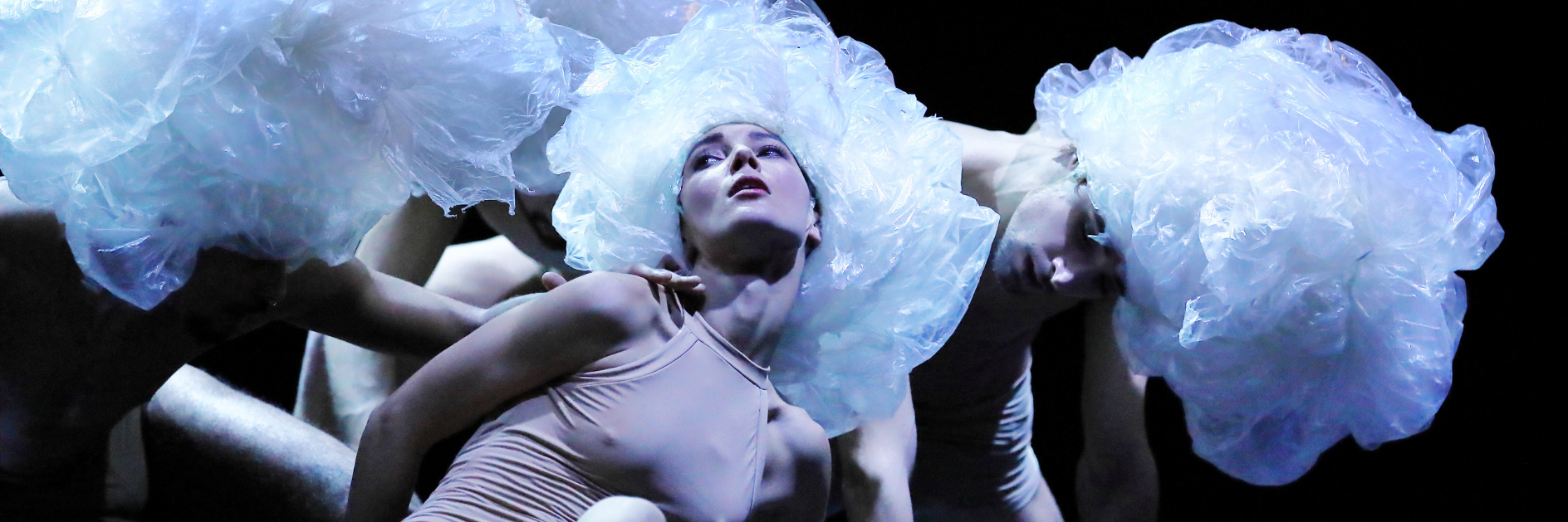 Tre ballerine distese a terra con body color carne e parrucche di plastica 