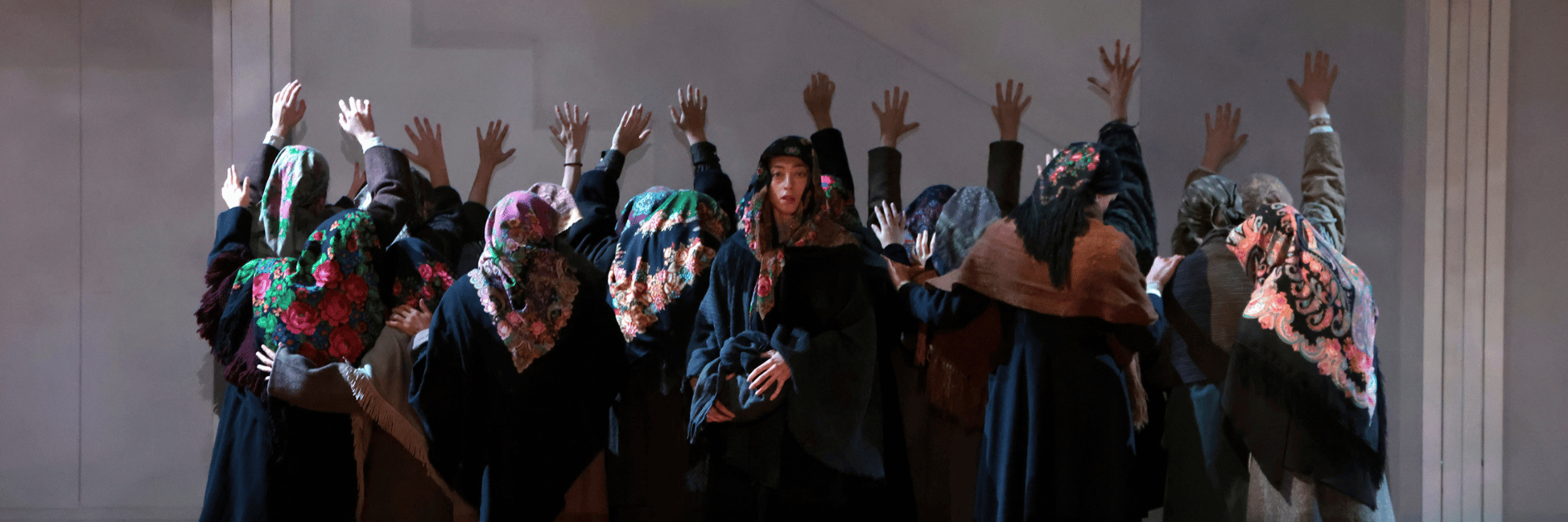 Foto di scena di un gruppo numeroso che alza le mani al cielo